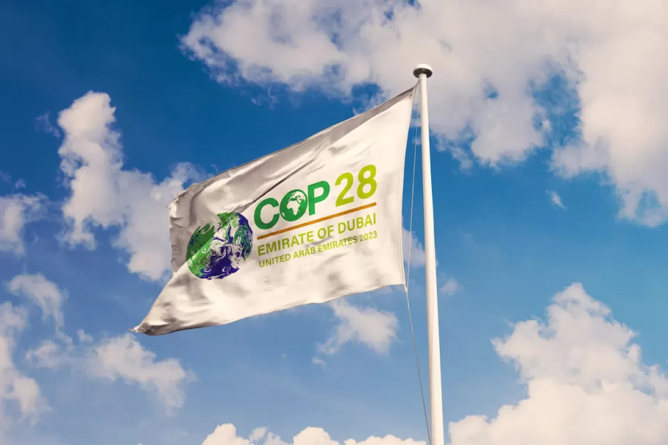 White flag with COP28 cliamte conference logo against lightly cloudy blue sky.